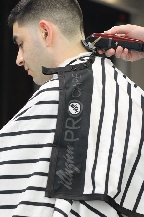 Barber giving a man a haircut, focused on the back of the neck. Black and white striped cape.