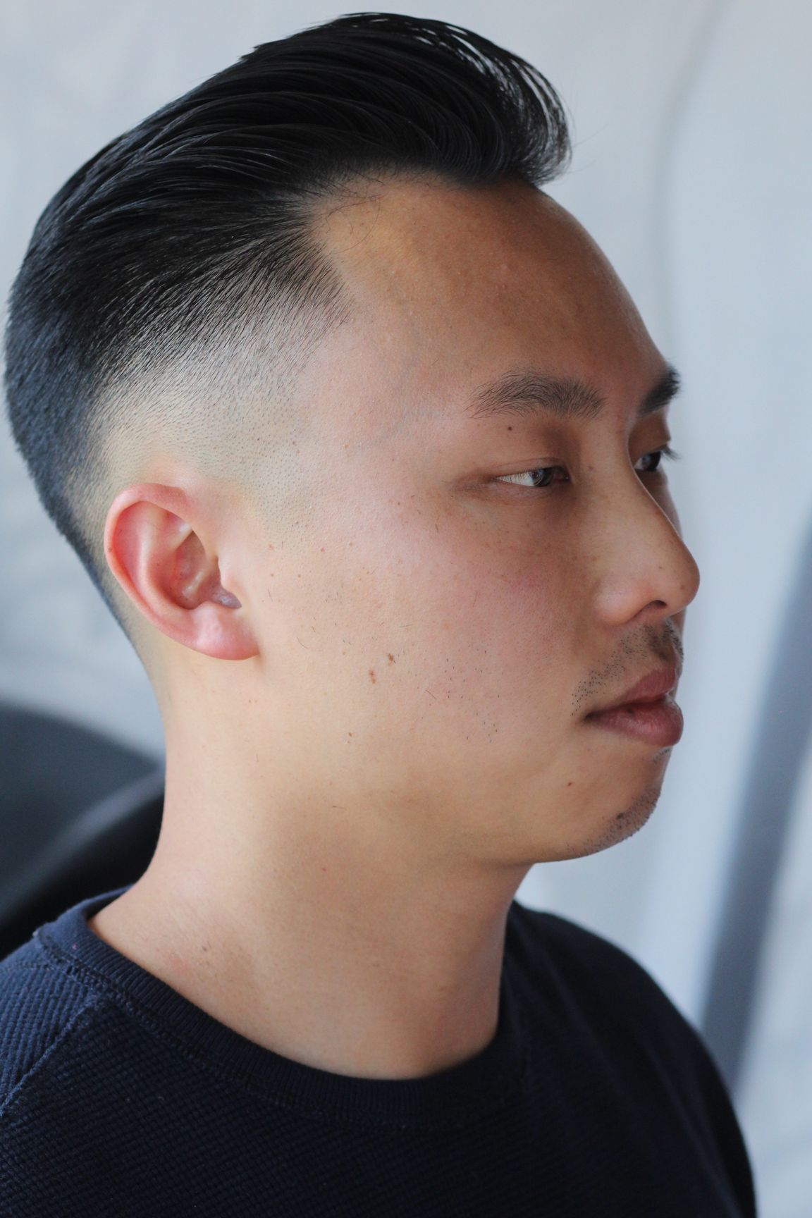 Asian man with a faded haircut, looking to the right, wearing a dark shirt.