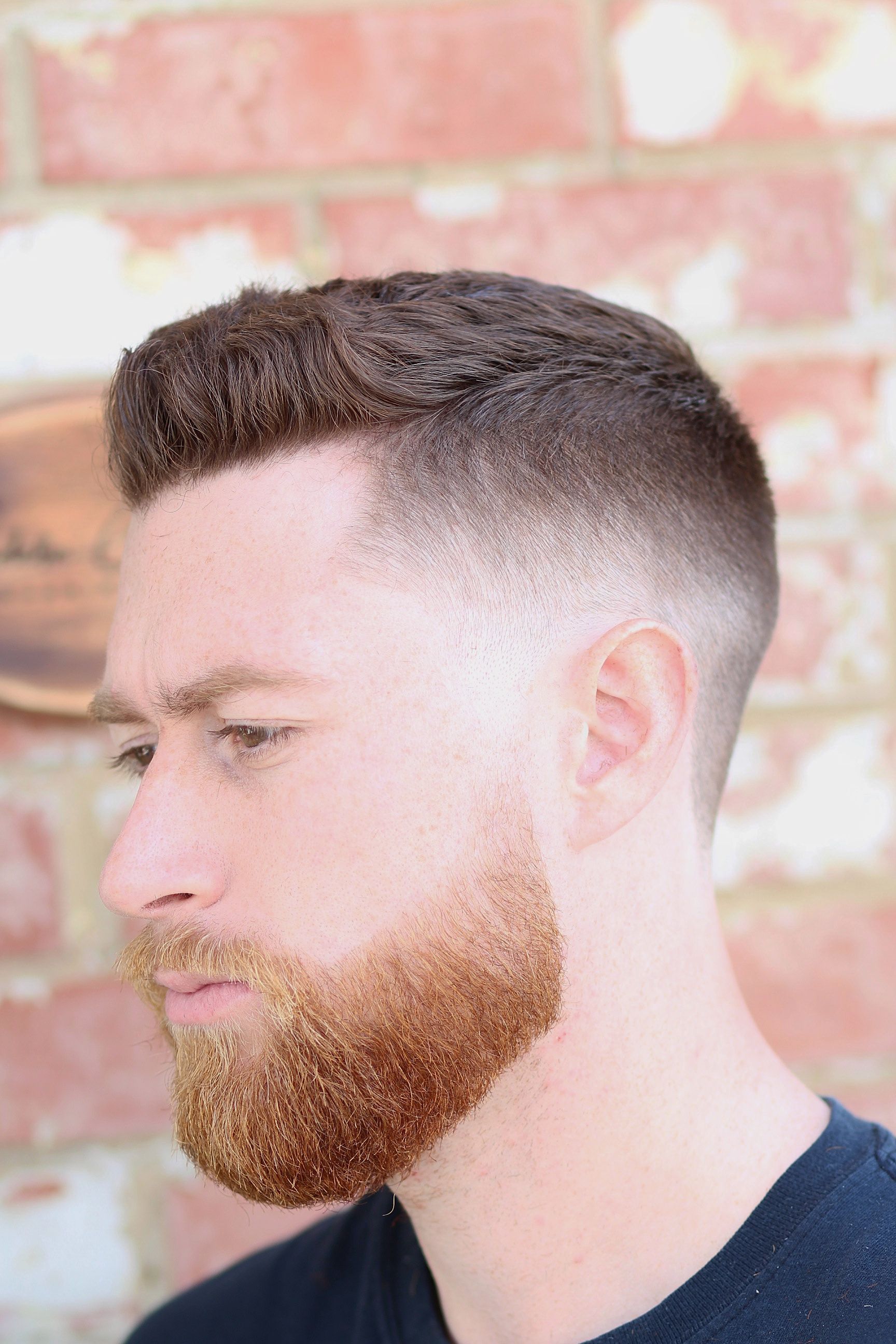 Man with a fade haircut and beard, against a brick wall.