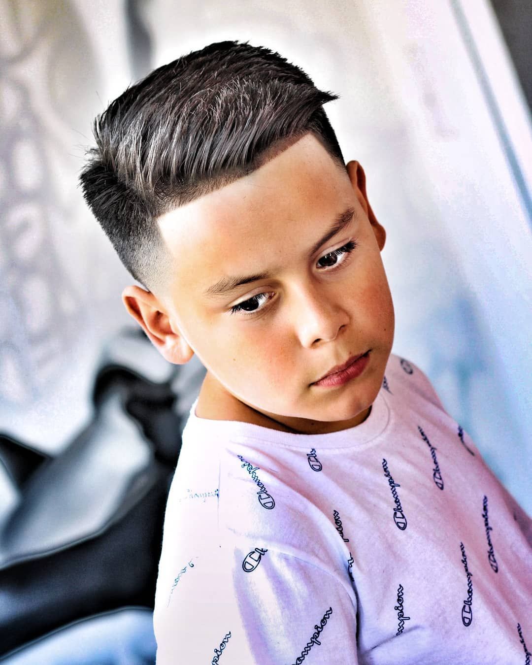 Boy with a fade haircut, wearing a white shirt, looking slightly down.