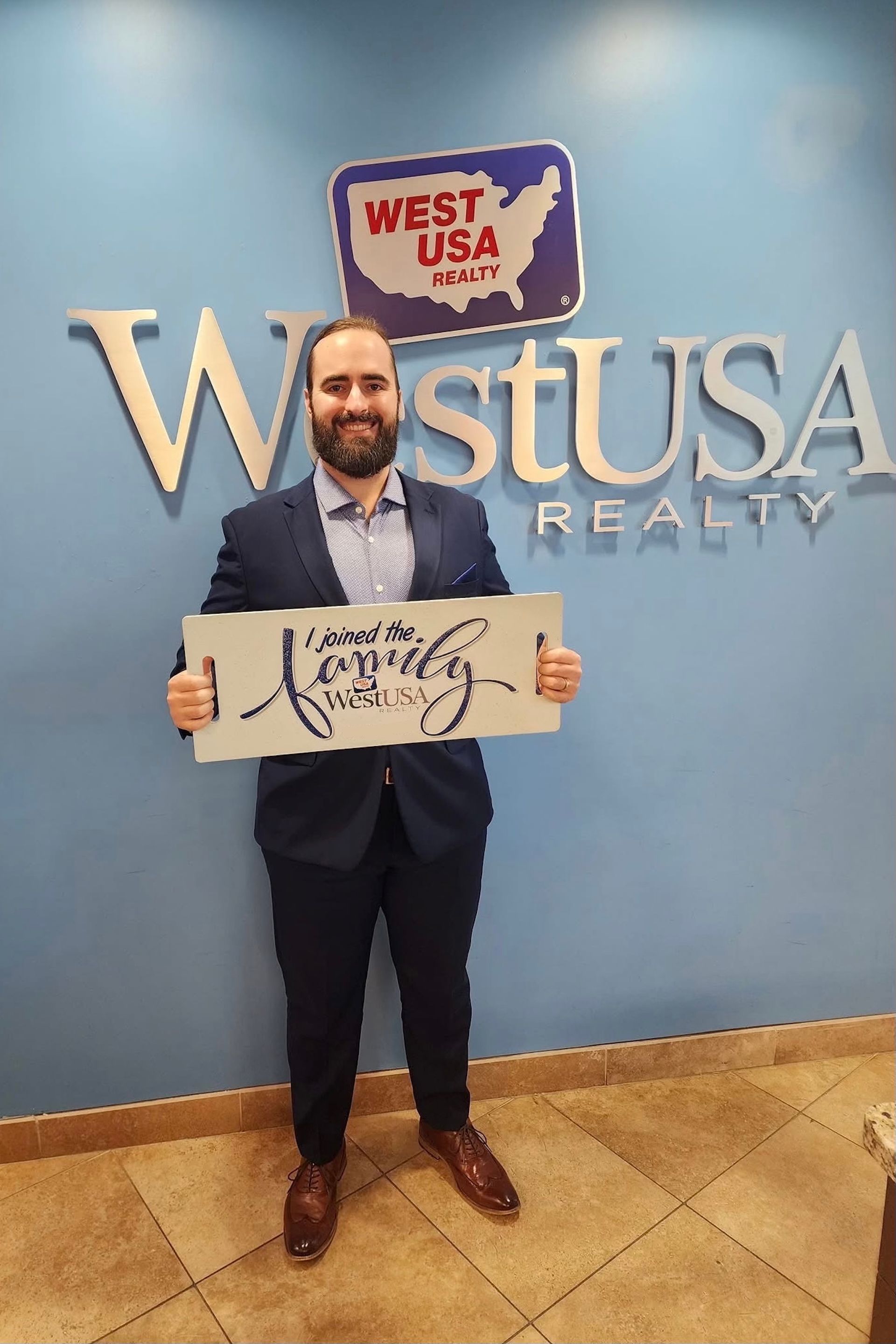 A man in a nice suit is standing in front of a sign that reads West USA Realty.