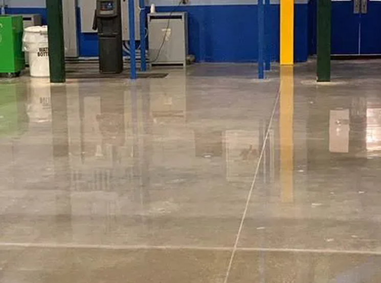 Shiny concrete floor in a warehouse-like space, with reflections of equipment and structural columns.