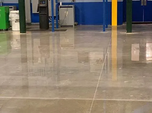 Polished concrete floor in an industrial setting, with reflections of walls and objects.