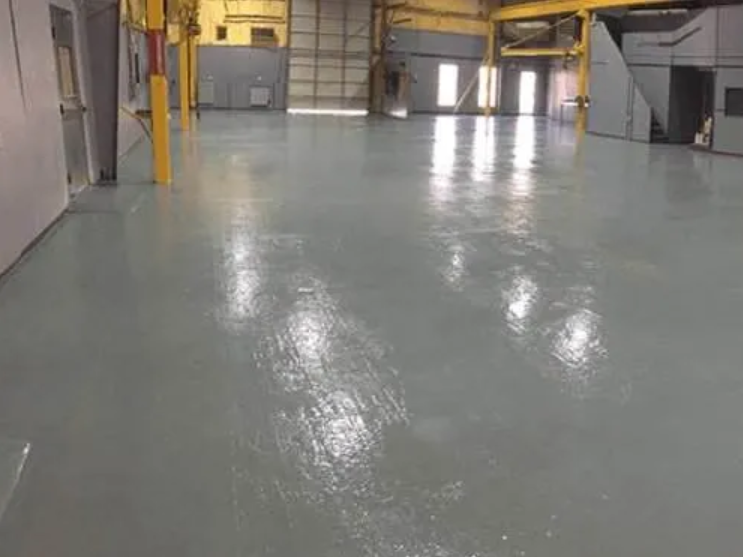 Gray epoxy-coated industrial floor, reflecting overhead lighting, in an open warehouse space.