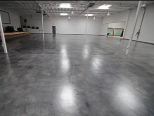 Empty gray-floored warehouse space with white walls, ceiling, and support beams.