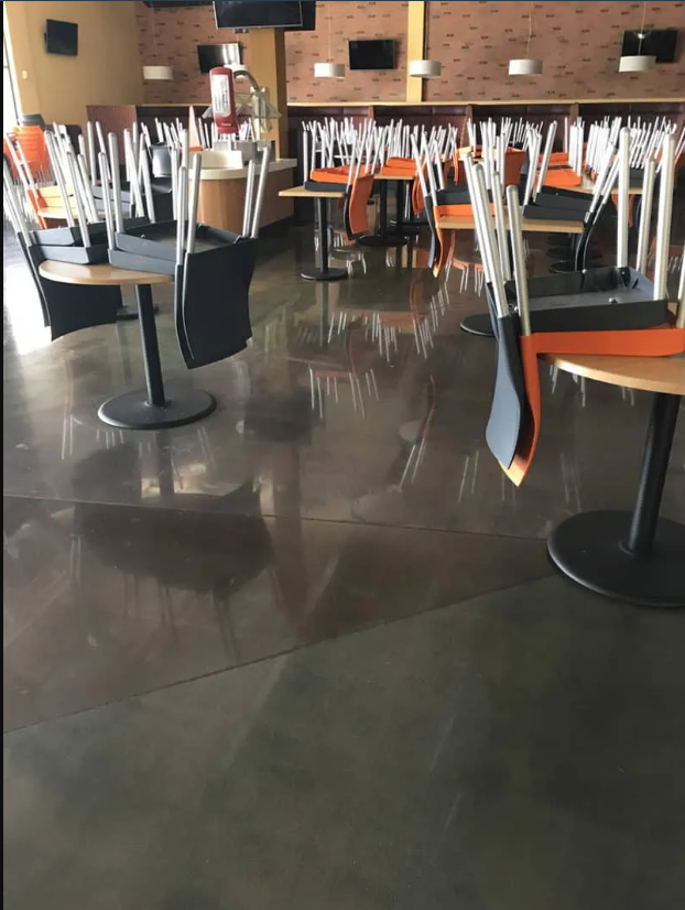 Restaurant interior with chairs upturned on tables, indicating closure. Polished gray floor.