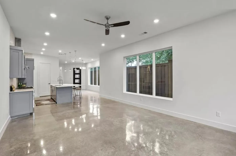 Open-concept living space with polished concrete floors, grey kitchen cabinets, large windows.
