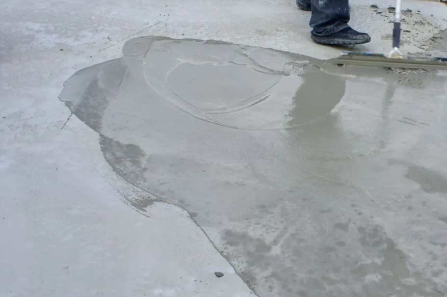 Person smoothing wet concrete on a gray surface with a trowel.