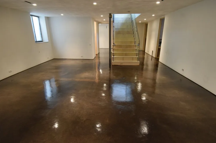 Empty room with shiny brown epoxy floor and stairs leading up.