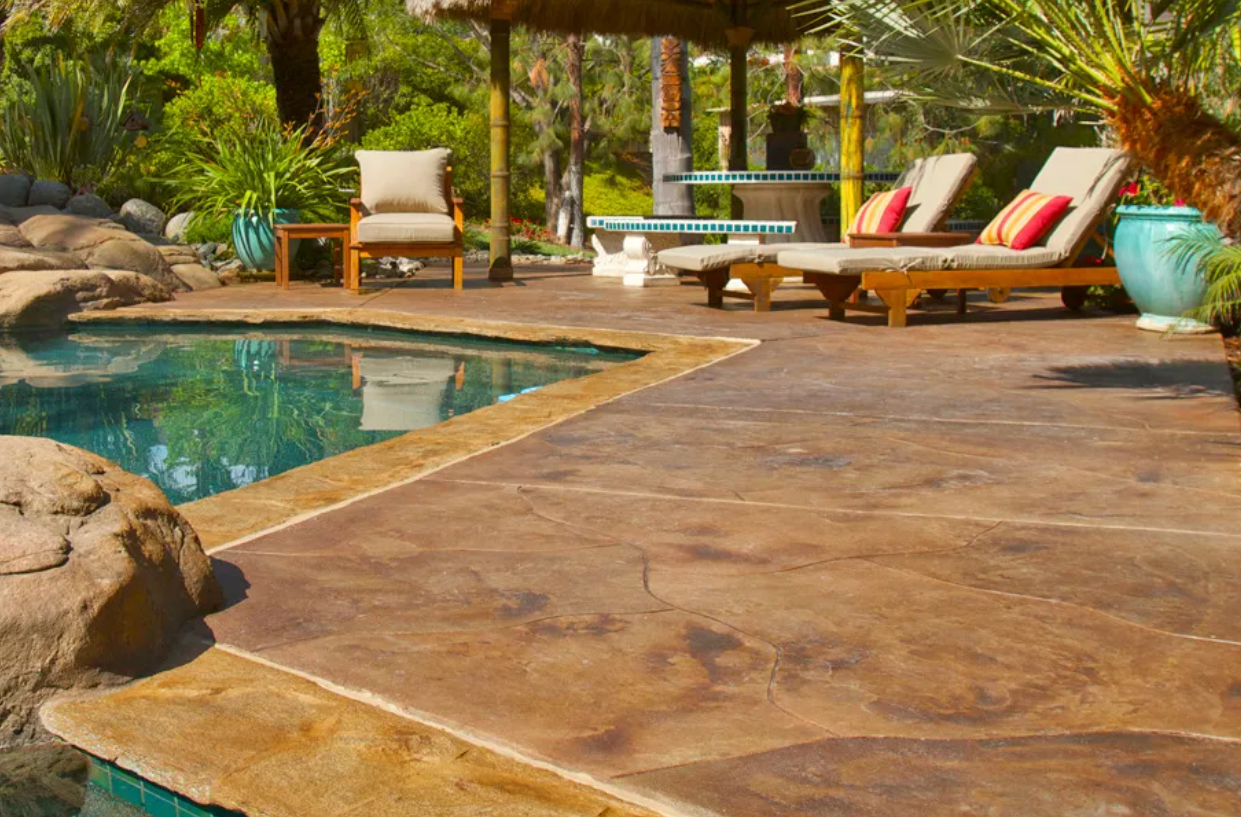 Poolside patio with chaise lounges, chair, and turquoise accents. Brown stamped concrete.