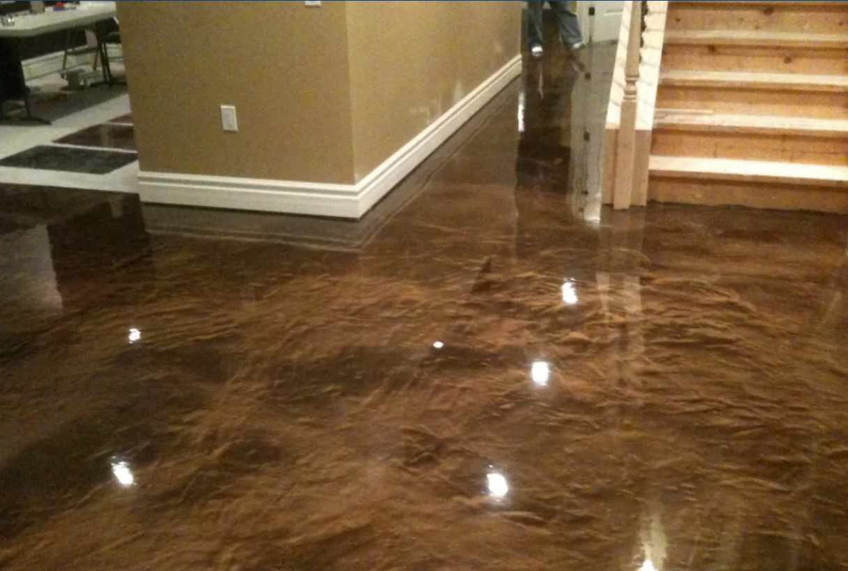 Brown metallic epoxy floor reflecting light in a home, next to a beige wall and wooden staircase.