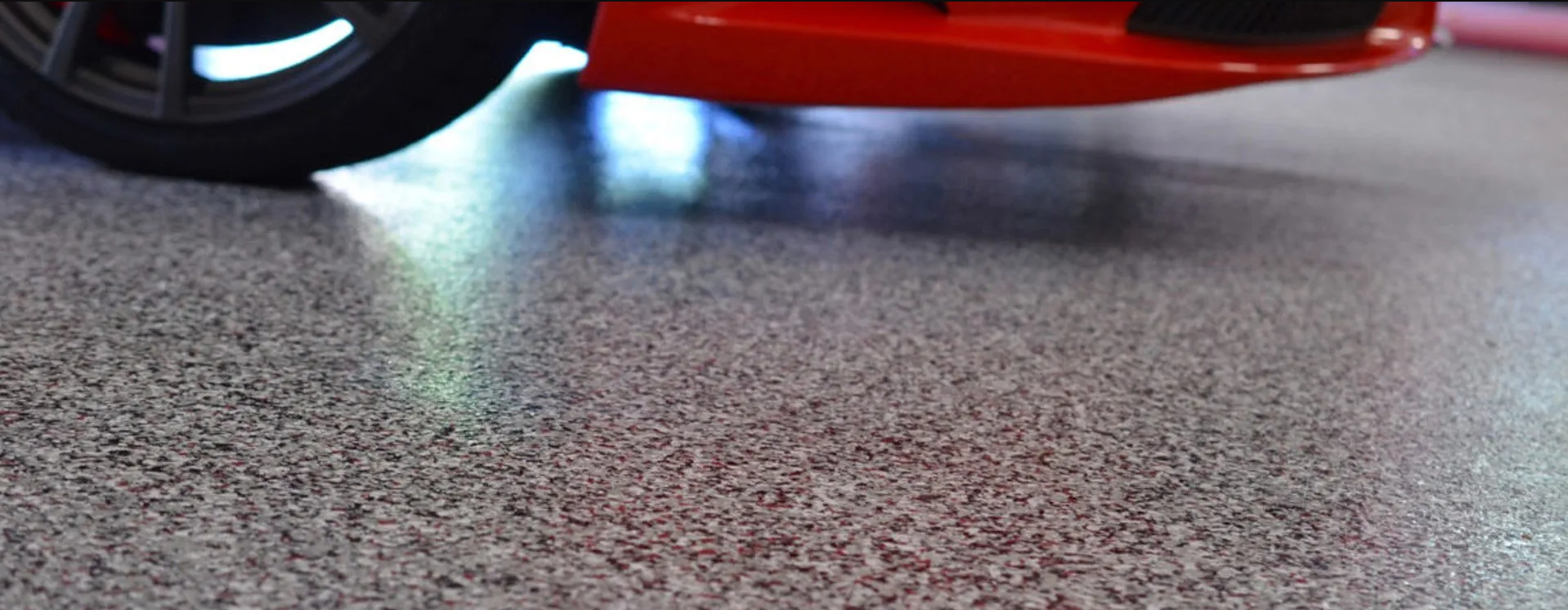 A red car with a black tire on a speckled gray floor.