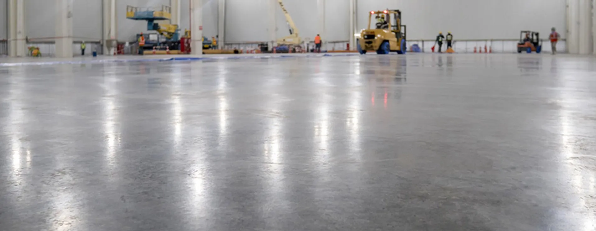 Large warehouse with a polished concrete floor, several people, and construction equipment.