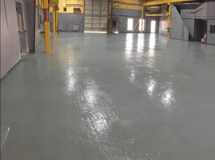 Gray, freshly painted industrial floor reflecting light inside a large warehouse.