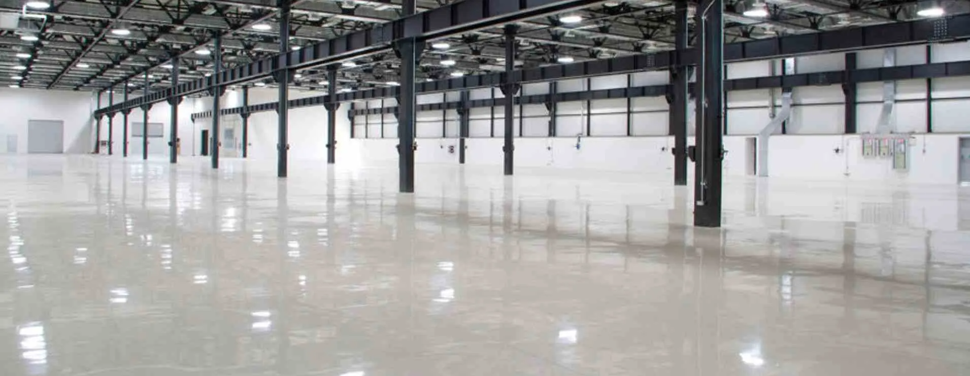 An empty warehouse interior with a highly polished floor reflecting lights and structural beams.