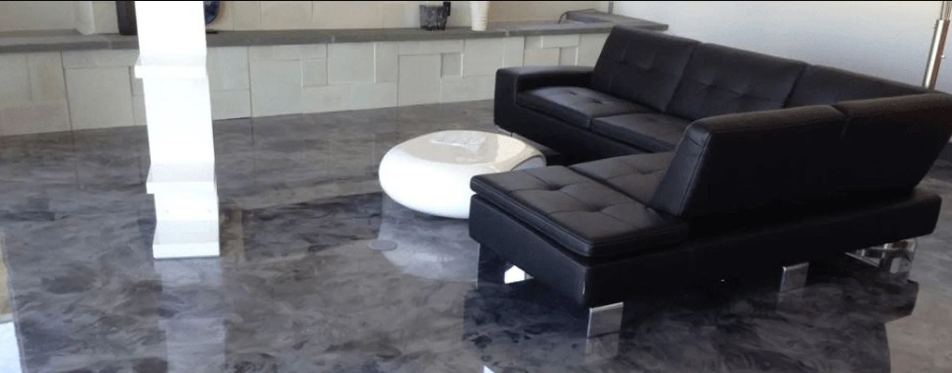 Black leather sectional sofa and white circular coffee table on a polished gray floor.