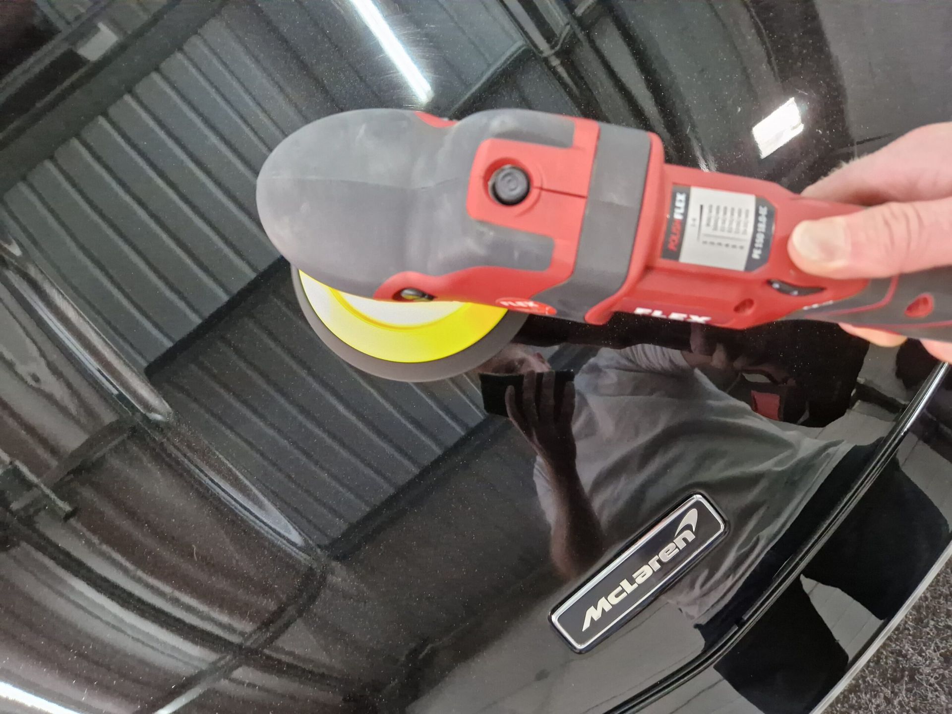 A person is polishing a mclaren car with a machine.