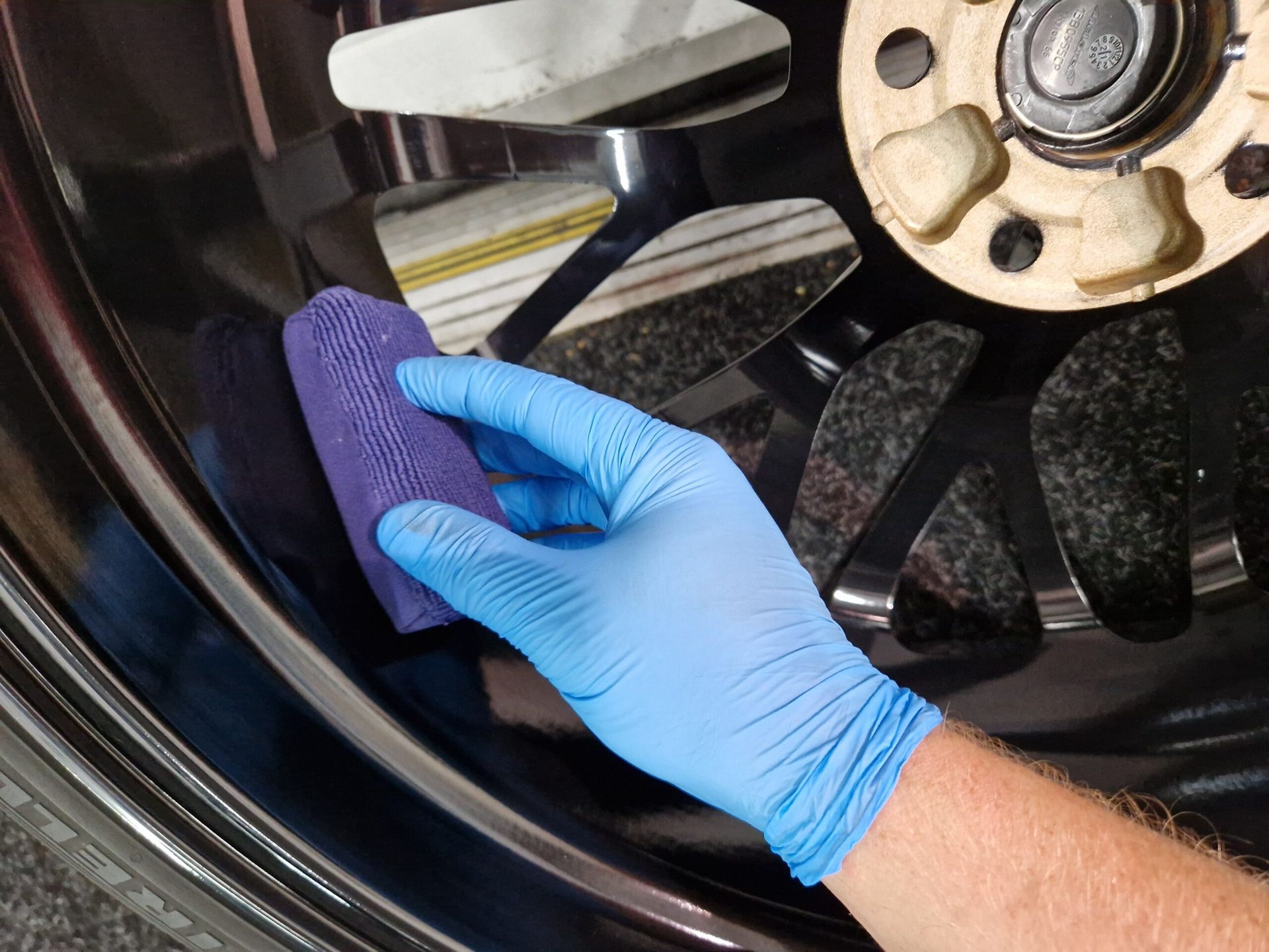 A person wearing blue gloves is cleaning a car wheel with a sponge.