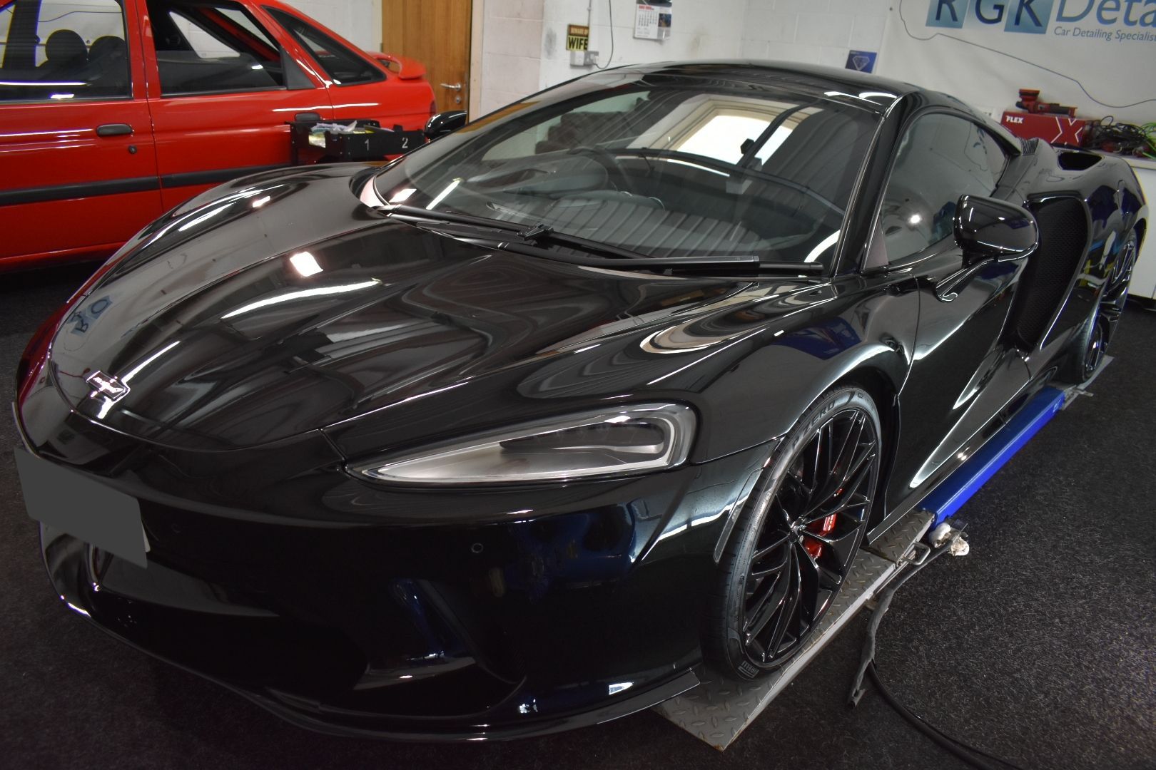 A black sports car is parked in a garage next to a red car.