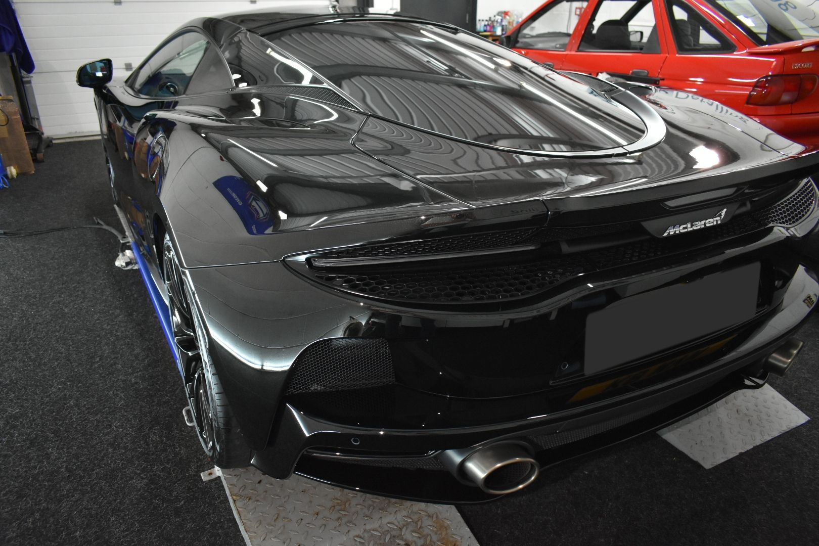 A black sports car is parked in a garage next to a red car.