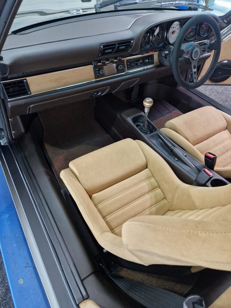 The interior of a blue car with tan seats and a steering wheel.