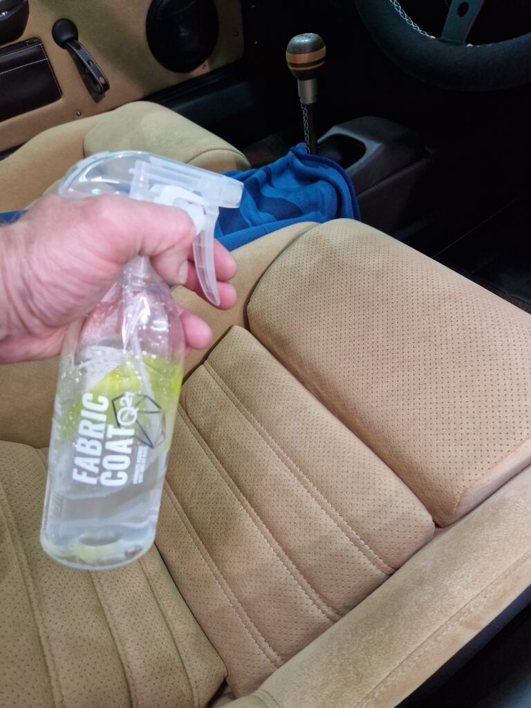 A person is holding a spray bottle that says fabric coat on it.