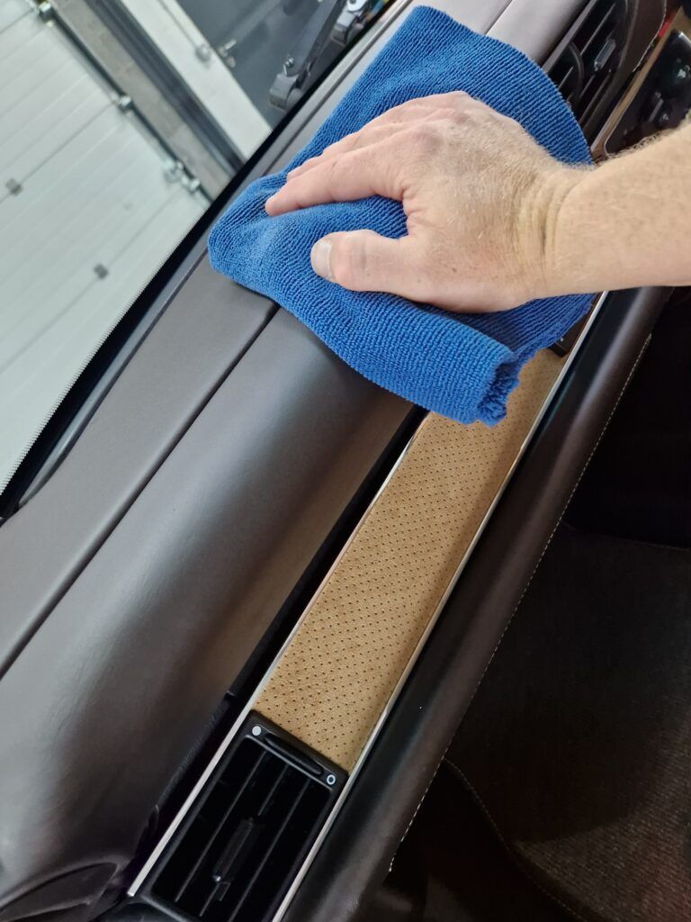 A person is cleaning the dashboard of a car with a blue cloth.