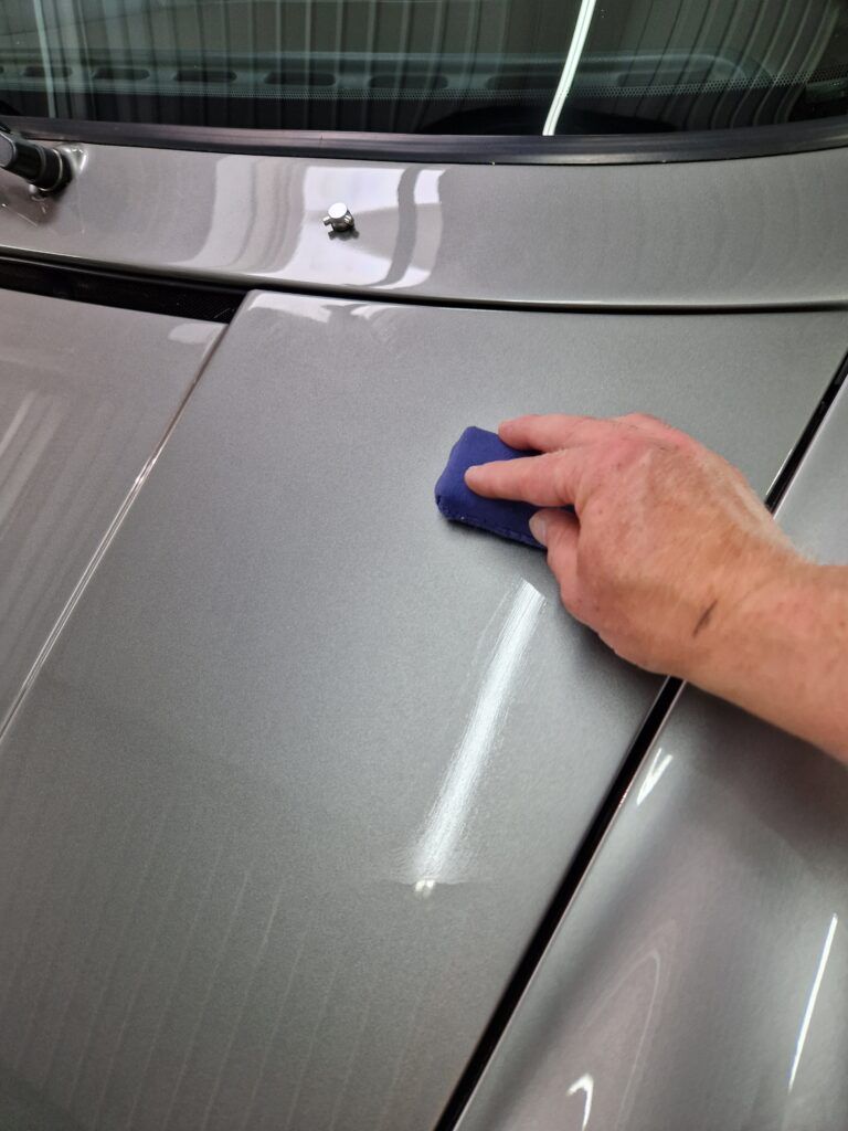 A person is cleaning the hood of a car with a blue sponge