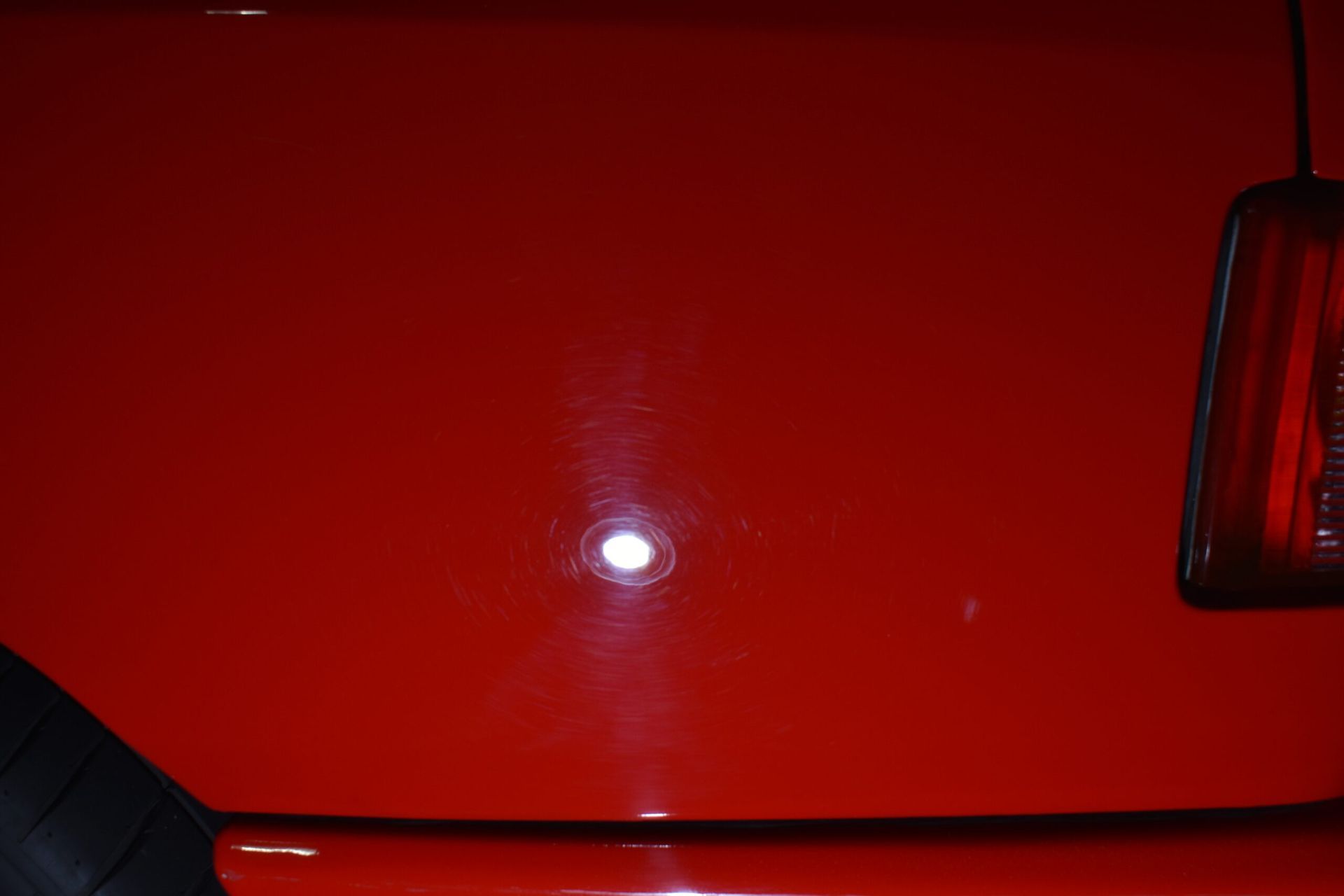 A close up of a red car 's hood and tail light.