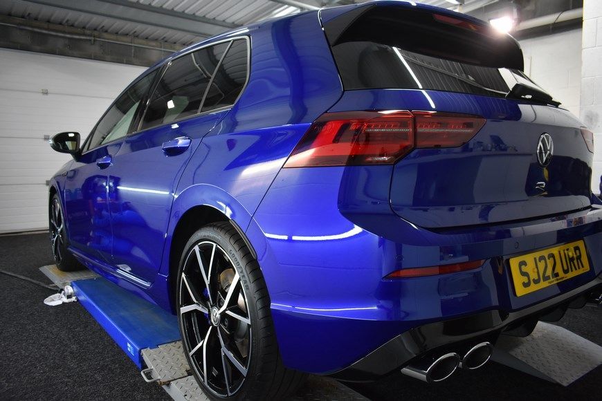 A blue volkswagen golf r is sitting on a lift in a garage.
