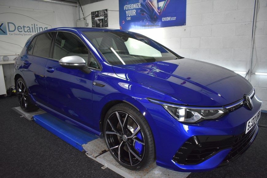 A blue volkswagen golf r is sitting on a lift in a garage.