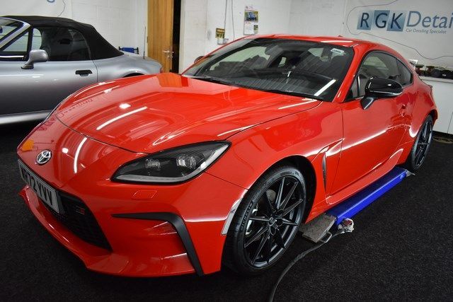 A red sports car is parked in front of a sign that says rgk detail