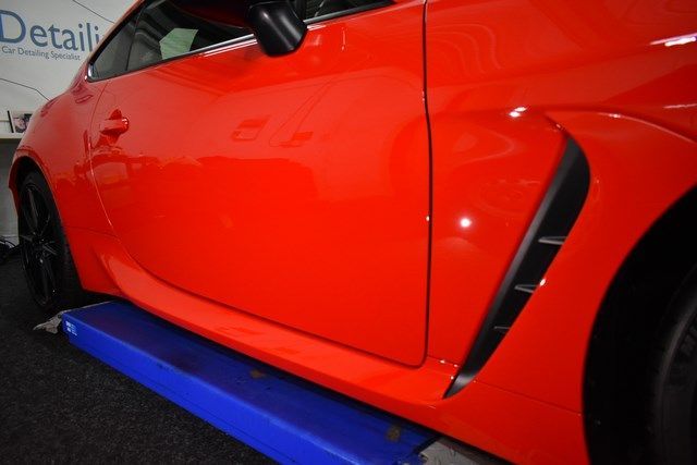 A red car is sitting on a lift in front of a sign that says detail