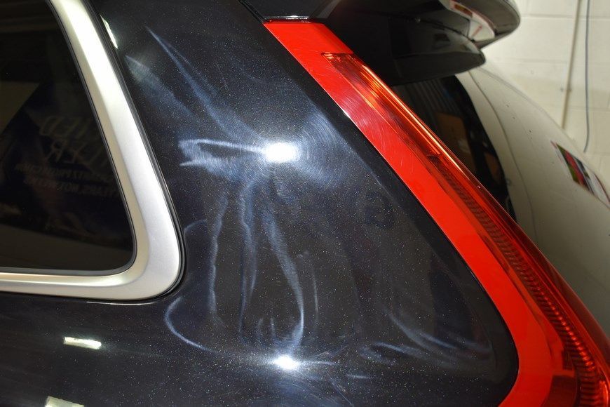 A black car with a red tail light is parked in a garage