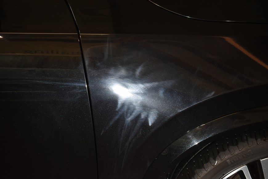A close up of a car 's fender with a lot of scratches on it.