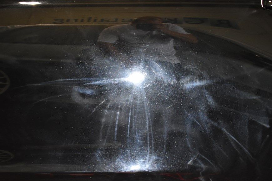 A man is taking a picture of his reflection in the windshield of a car