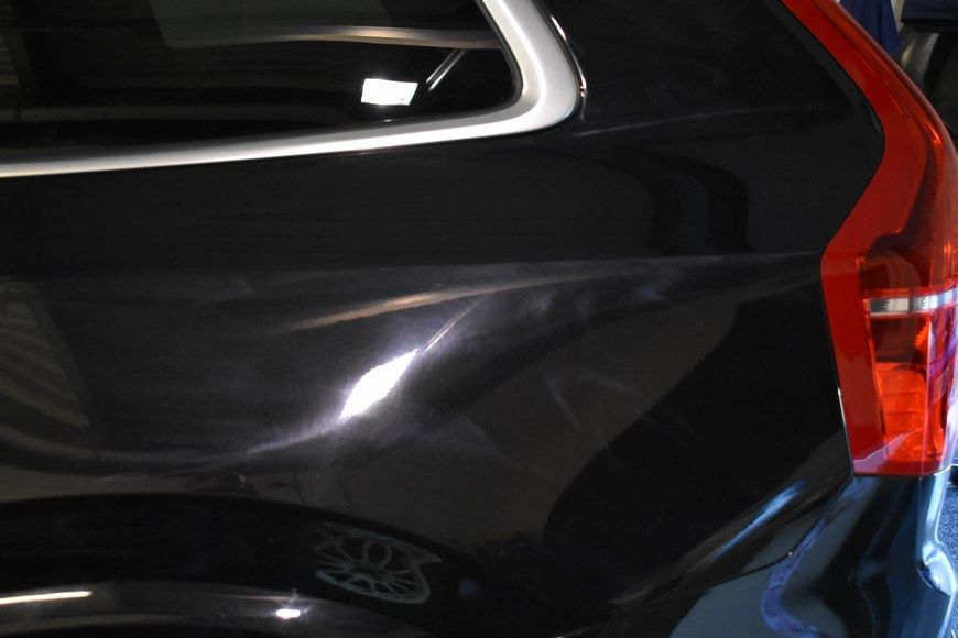 A black car with a red tail light is parked in a garage