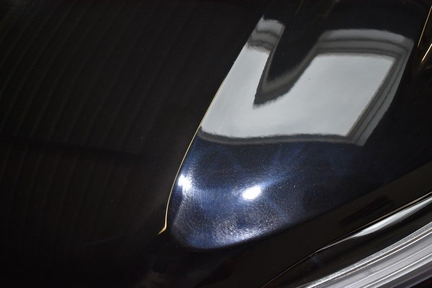 A close up of a car hood with a reflection of a building in it.