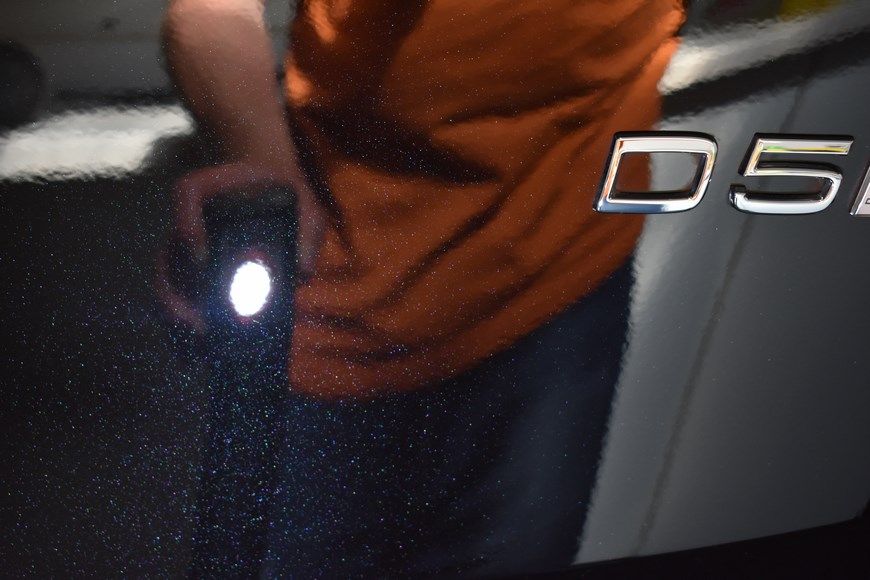 A person is holding a flashlight in front of a car with the letter d on it.