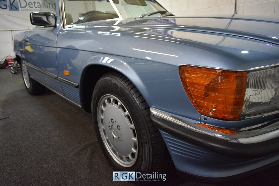 A blue car is parked in front of a sign that says rgk detailing