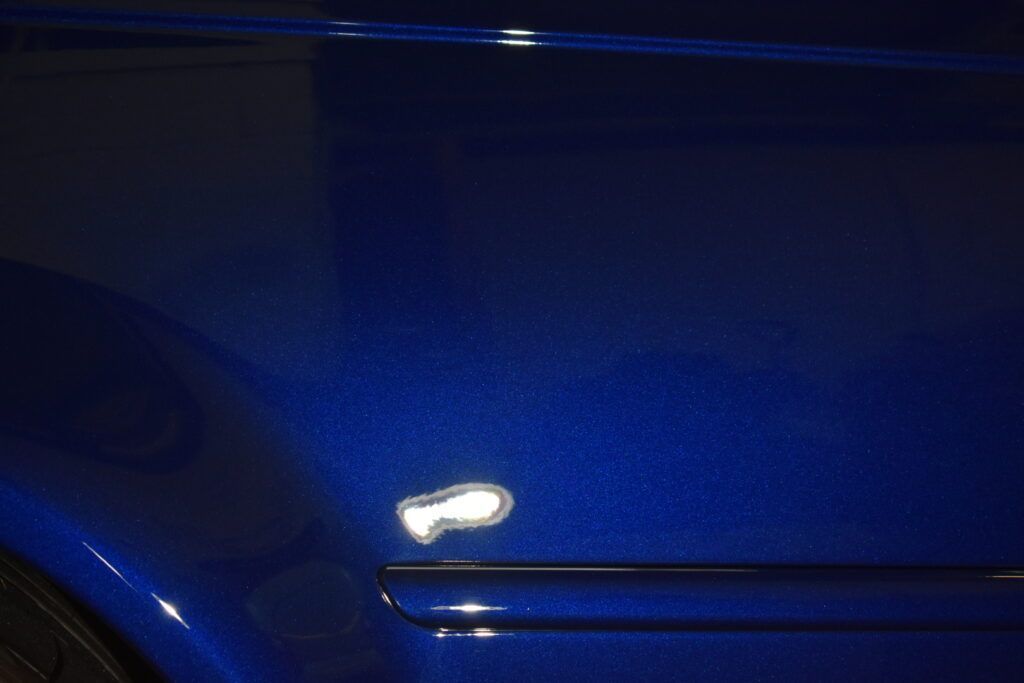 A close up of a blue car door with a white spot on it.