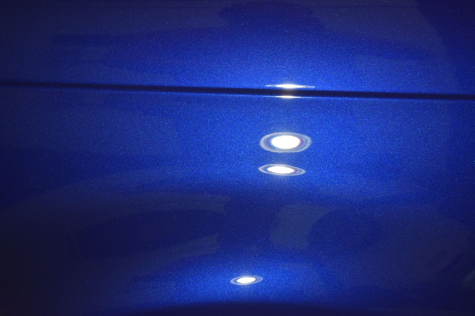 A close up of a blue car with a reflection of lights on it.