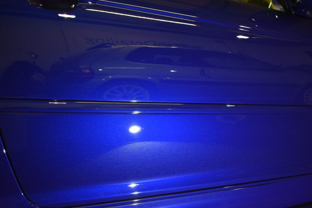 A blue car is parked in a parking lot at night.