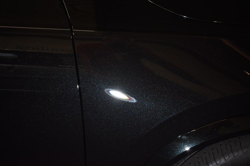 A close up of a black car 's fender in a dark room.