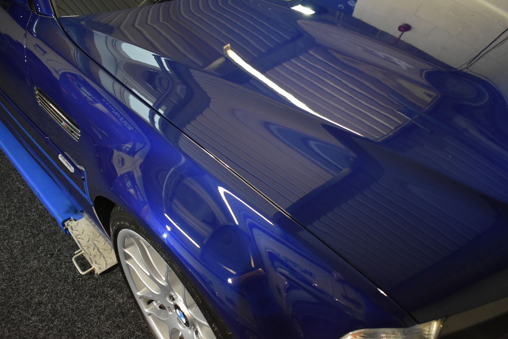 A blue car is parked in a garage with the hood up.