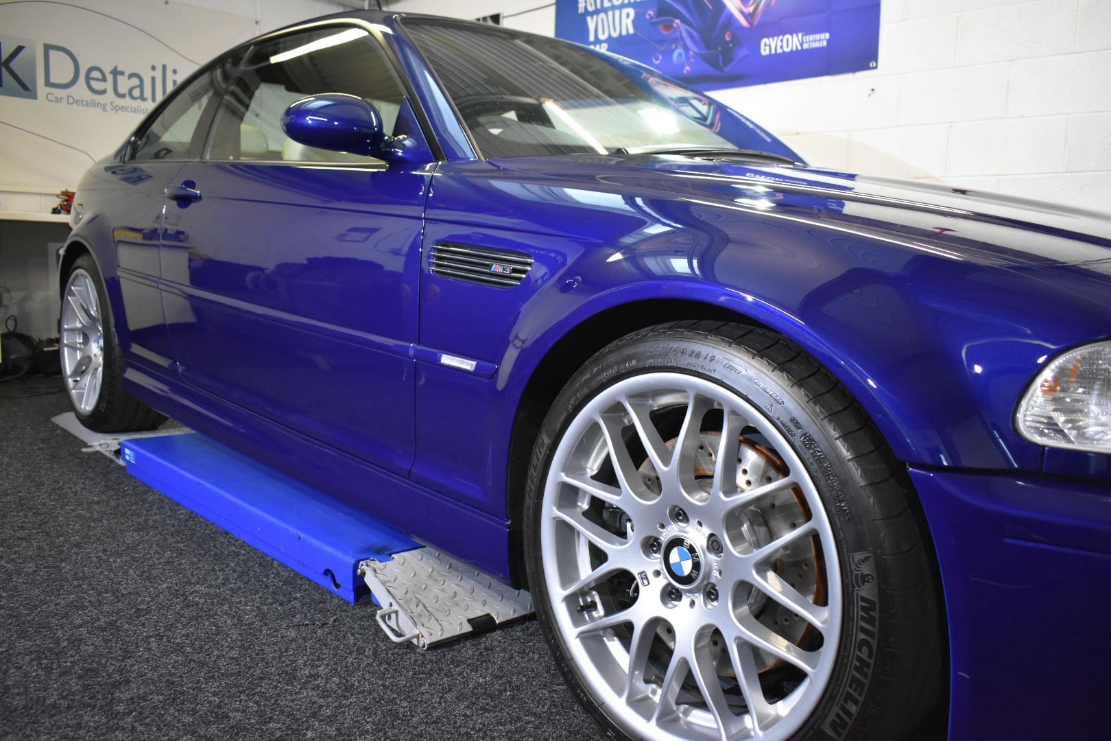A blue bmw m3 is sitting on a lift in a garage.