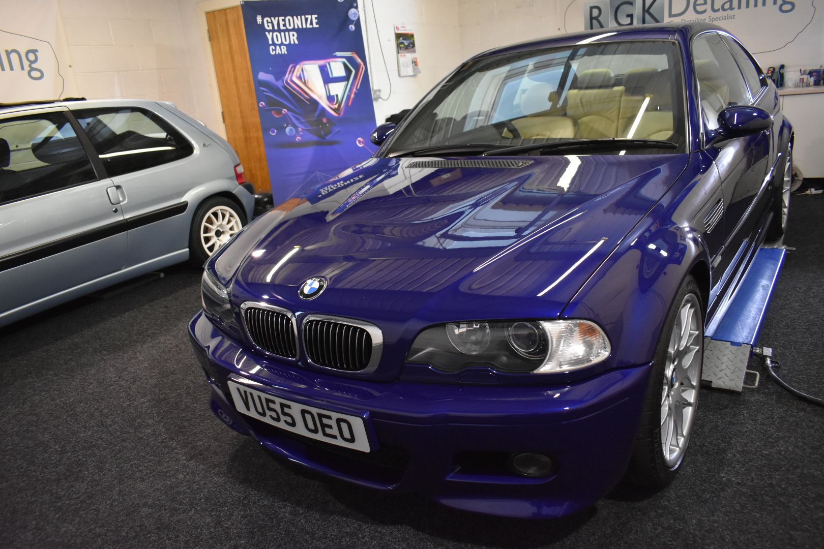 A purple bmw is parked in a garage next to a silver car.