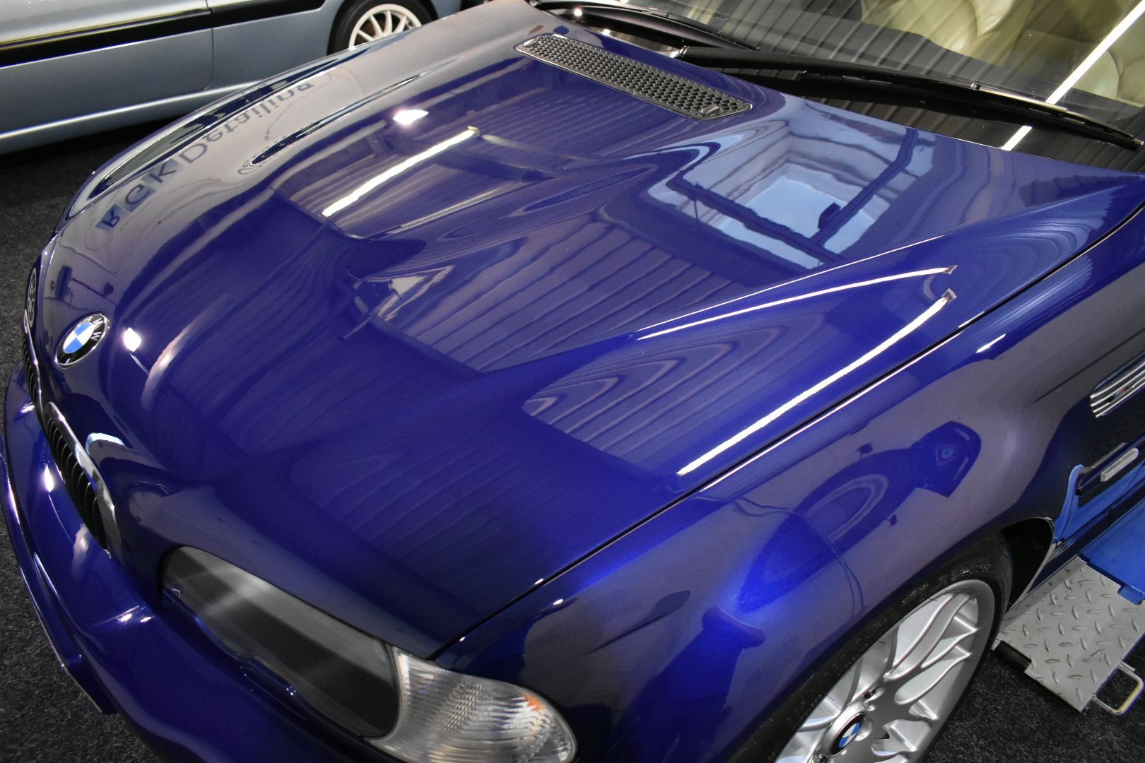 A blue bmw is parked in a garage with the hood up