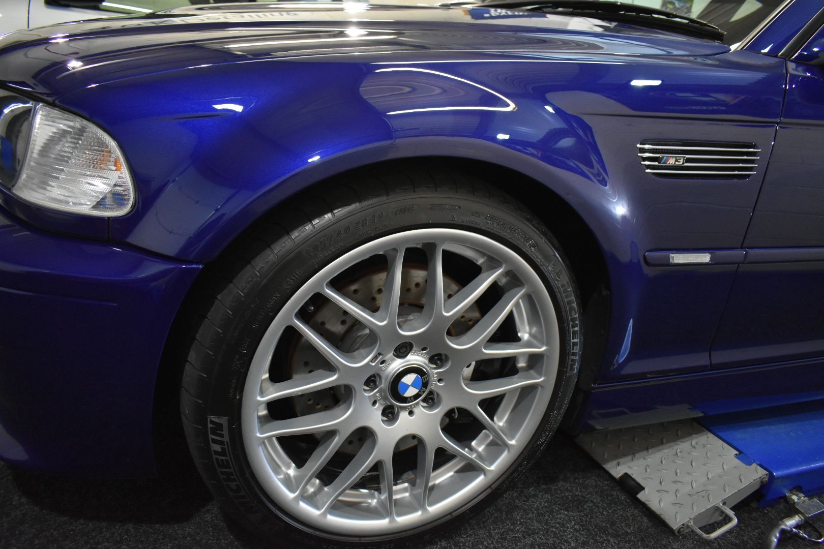 A blue bmw m3 is sitting on a lift in a garage.