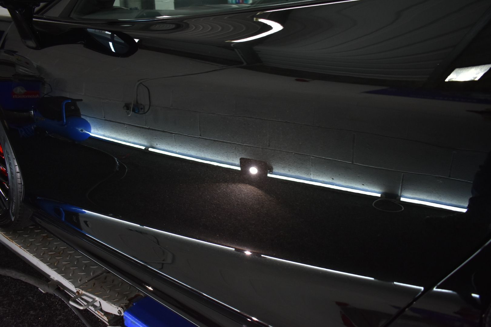 A black car is parked in a dark room with a light on the side of it.